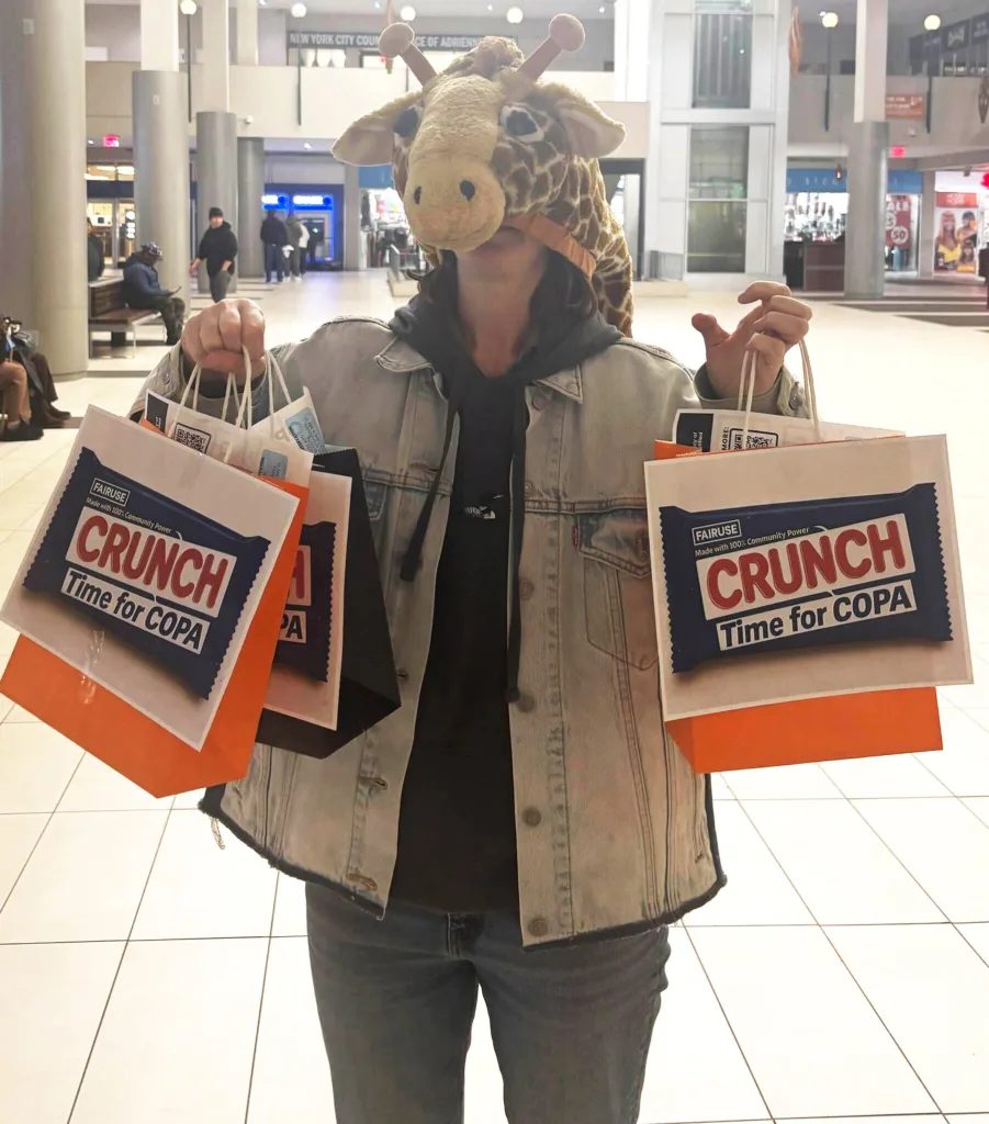 A person in a giraffe costume holding bags with a candy bar reading "Crunch time for COPA"