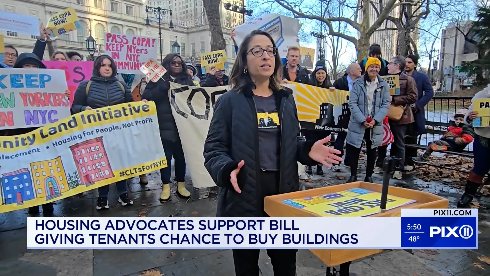 Executive Director Deyanira Del Rio speaks in front of a group of COPA supporters holding signs and banners.