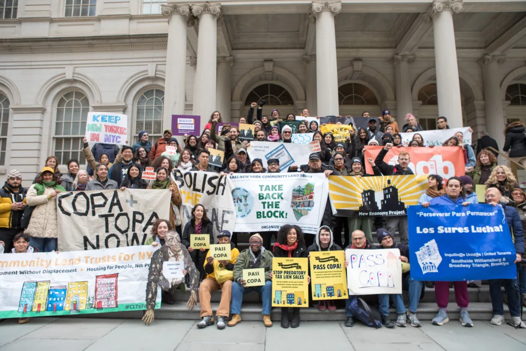 A large group of people on the steps of New York City Hall, holding signs at a rally in support of COPA.